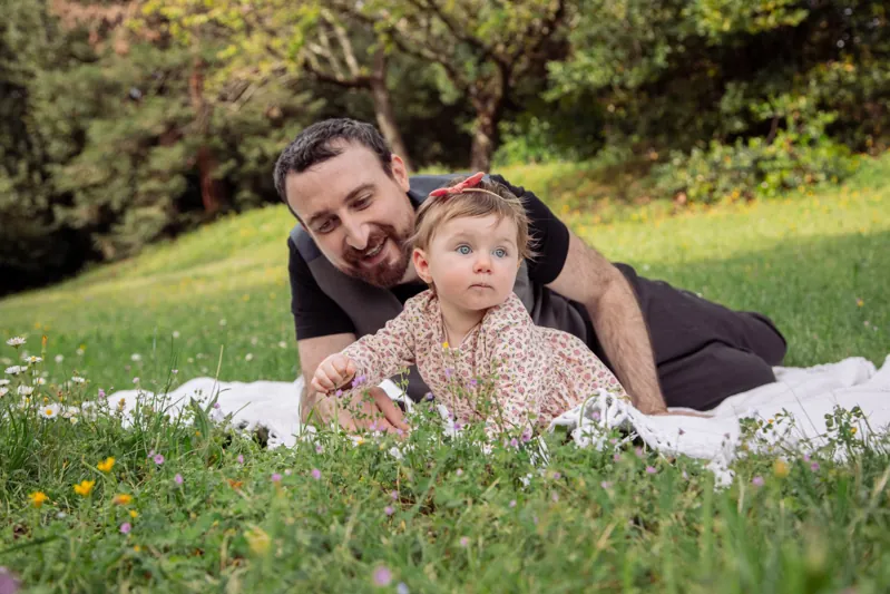 Un papà e una mamma giocano con la loro bambina su una coperta nel prato